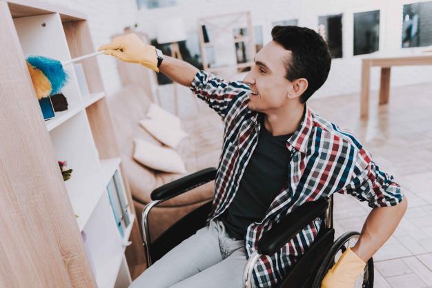 Man in wheelchair dusting a bookshelf